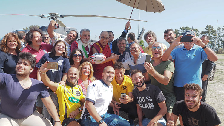 Seine Heiligkeit der Dalai Lama bei einem Gruppenfoto mit dem Sonntag-Rugby-Team, dessen Trainingsgelände als Hubschrauber-Platz für die Reise nach Palermo diente – in Messina, Sizilien, Italien, am 17. September 2017. Foto: Jeremy Russell