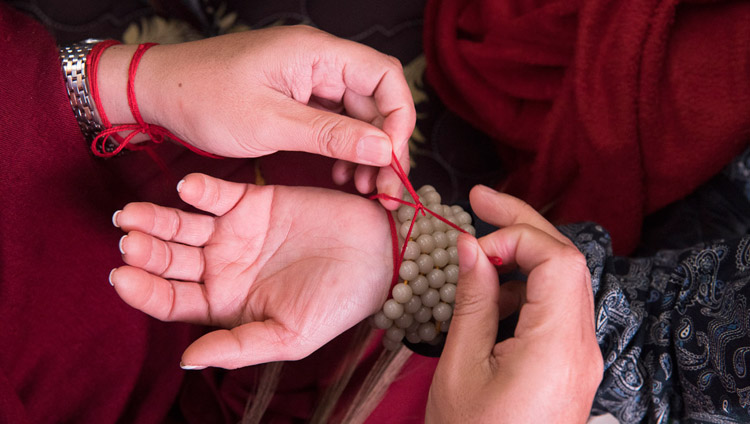 Teilnehmende binden sich rituelle Schutzschnüre um ihr Handgelenk während des Vorbereitungsrituals für die anstehenden Ermächtigungen durch Seine Heiligkeit den Dalai Lama in Bodhgaya, Bihar, Indien am 18. Januar 2018. Foto: Manuel Bauer