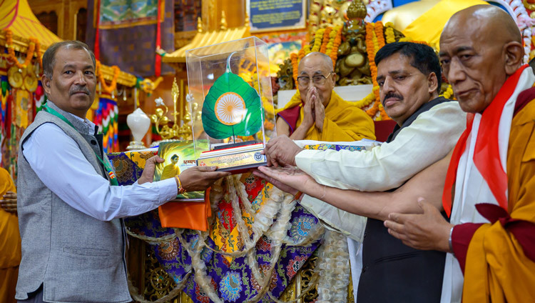 Zwei Laienvertreter des Himalaya-Buddhistischen Kulturvereins überreichen Seiner Heiligkeit dem Dalai Lama ein gerahmtes, verziertes Bodhi-Blatt während des Langlebensgebets im tibetischen Haupttempel. Dharamsala, HP, Indien, 20. Mai 2026. Foto: Tenzin Choejor
